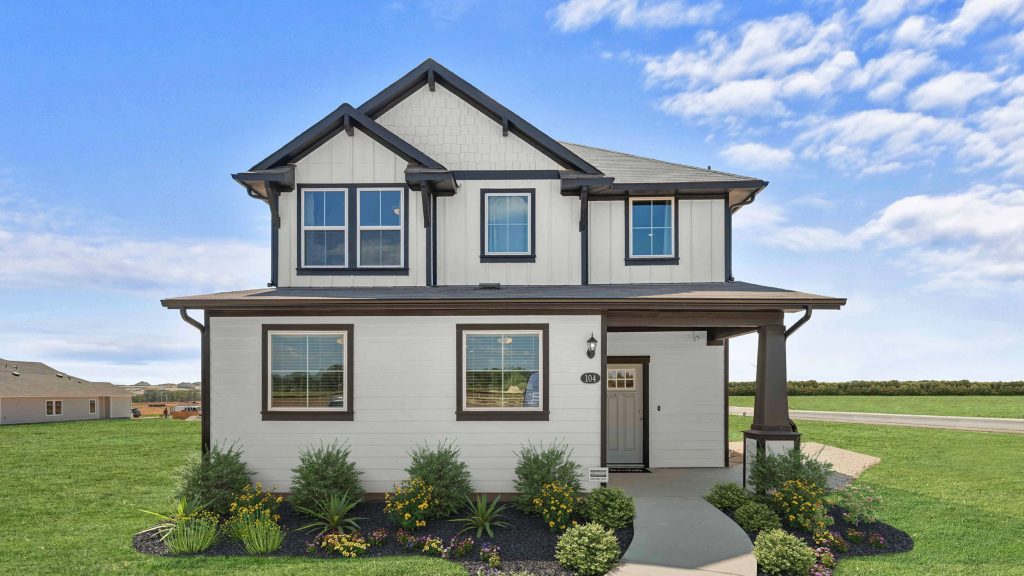 Image of front exterior of two-story house with grass landscape, bushes, flowers, blue sky with clouds, and concrete sidewalk.