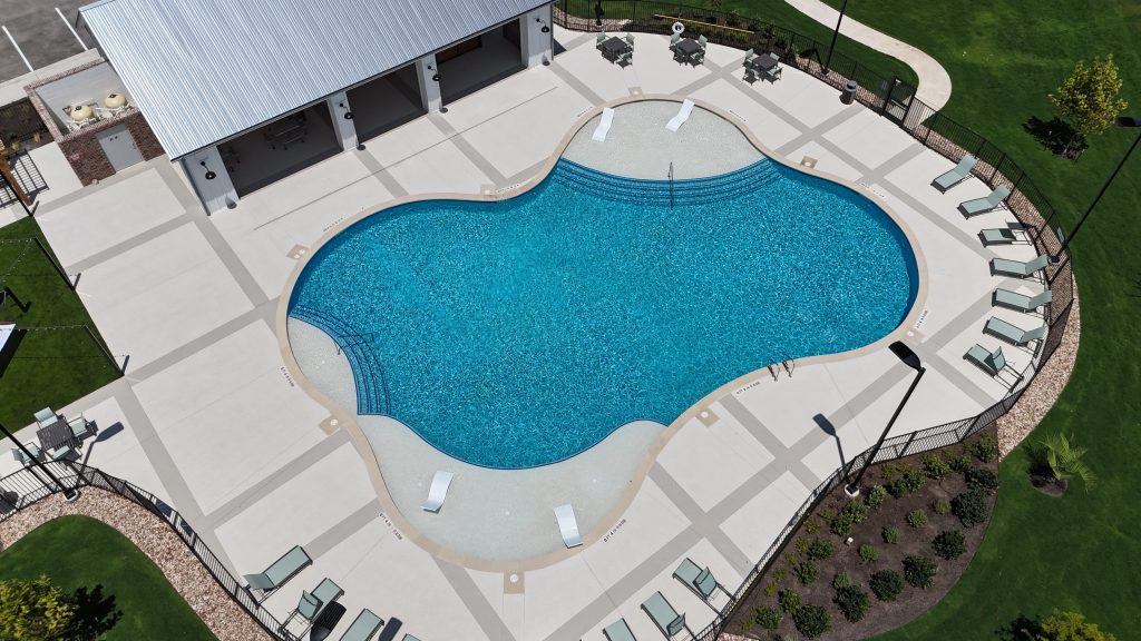 Aerial photo of community pool surrounded by a pool deck with lounge chairs and pavilion on one side