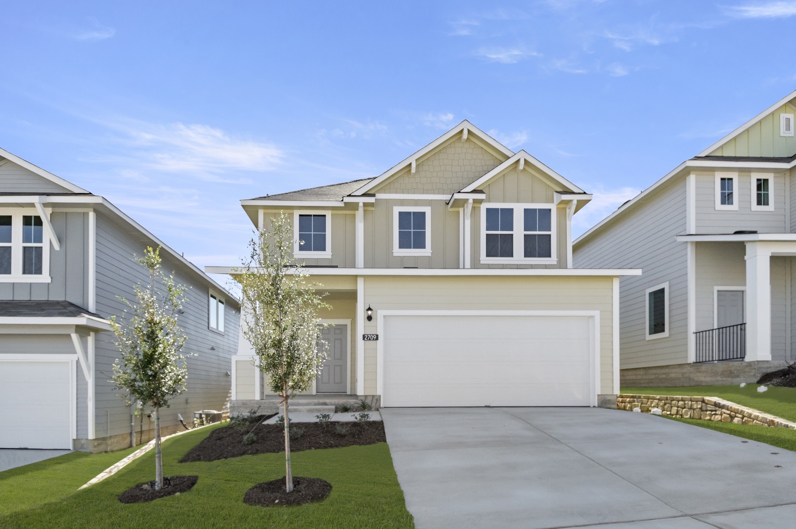 Image of the exterior beige two story home with a white two car garage and a cement driveway and green grass and a blue sky
