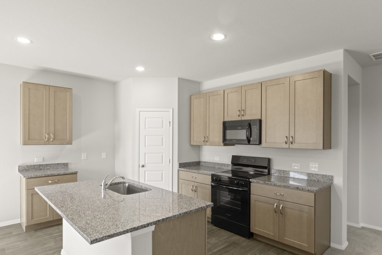 Image of a kitchen with light brown cabinets and island with granite countertops and black appliances