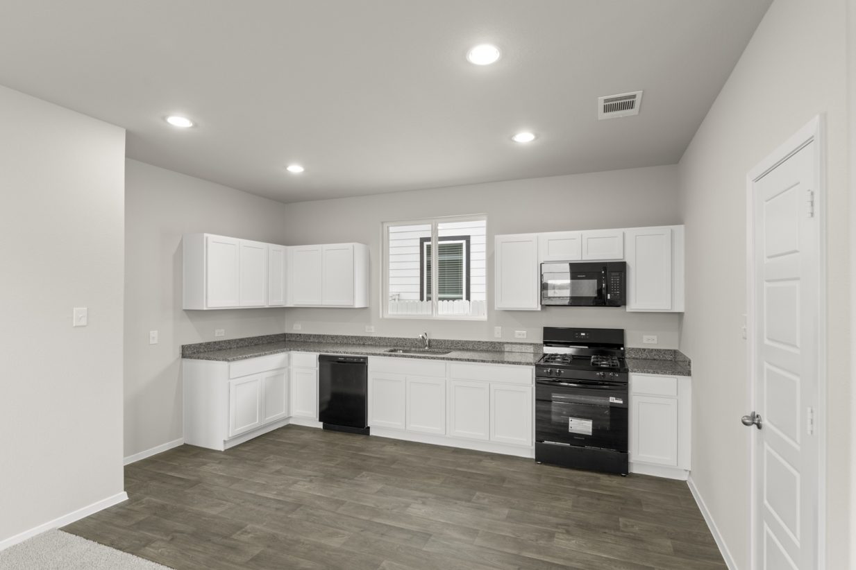 Image of a kitchen with white cabinets, brown vinyl flooring, granite countertops, black appliances and a window above the sink