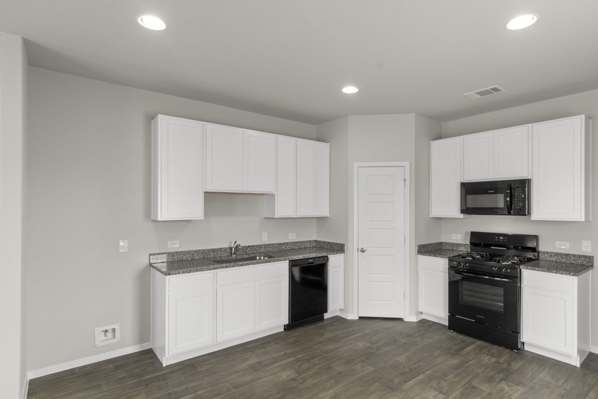 An image of a kitchen with wood vinyl flooring, cream colored walls, white cabinets with grey countertops, and black appliances.
