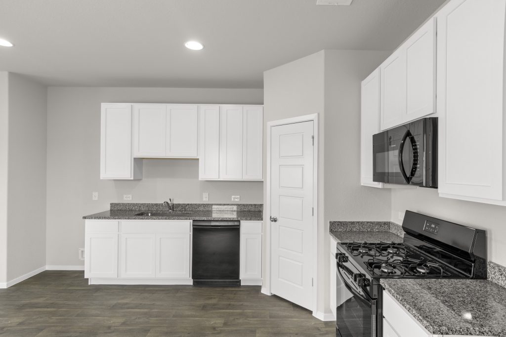 An image of a kitchen with wood vinyl flooring, cream colored walls, white cabinets with grey countertops, and black appliances.