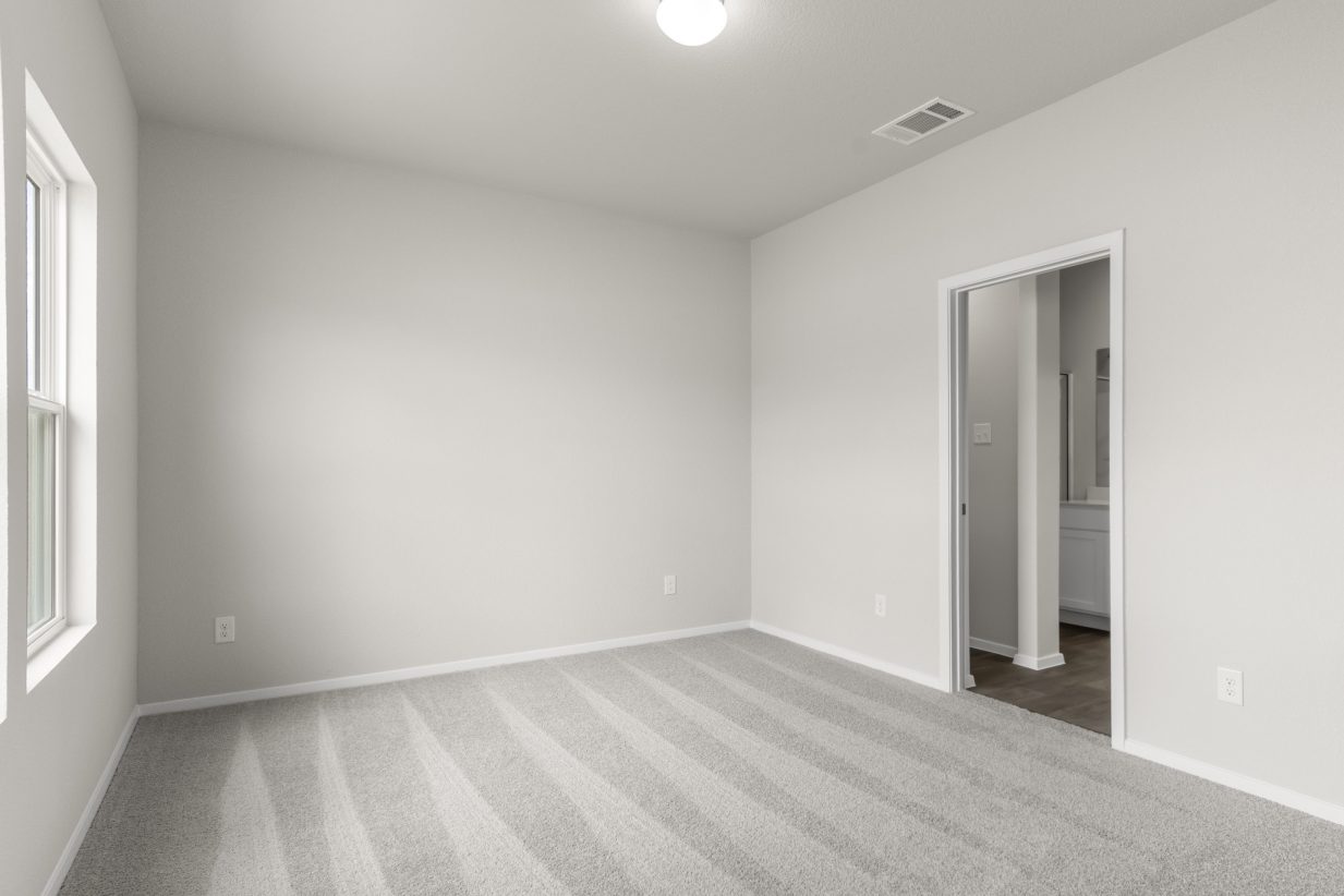 A image of a bedroom with cream color painted walls, white framed windows, a white door, and carpet flooring.