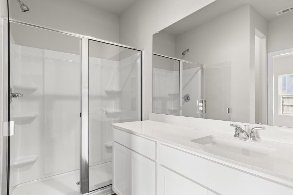 An image of a bathroom with a white vanity with white countertops, glass showers with white tile, and cream colored painted walls.