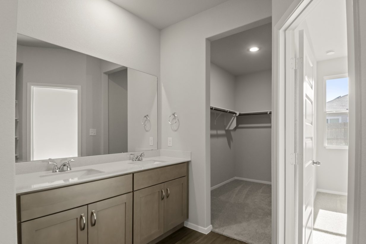 Image of a primary bathroom with brown cabinets and a jack and jill vanity with a large mirror and an attached walk-in closet