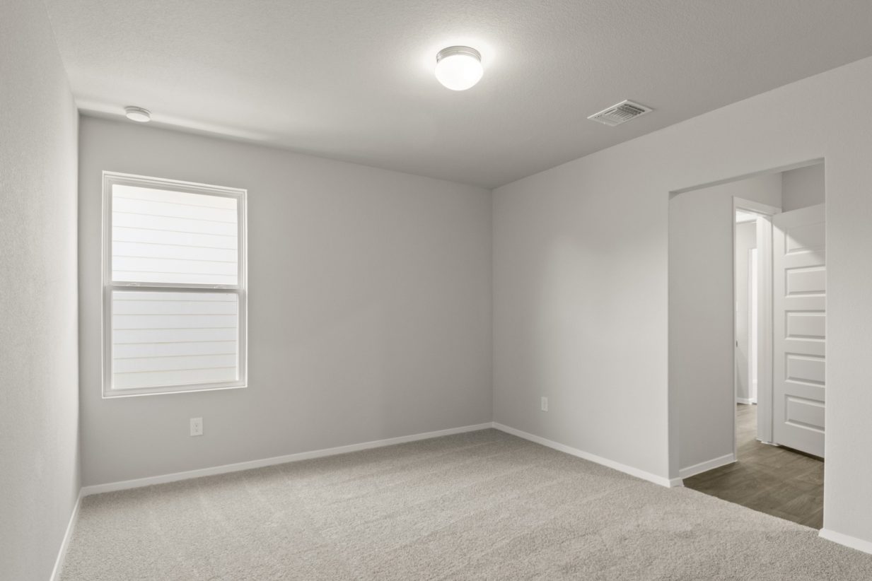 Image of a bedroom with tan carpeting and light grey painted walls with windows