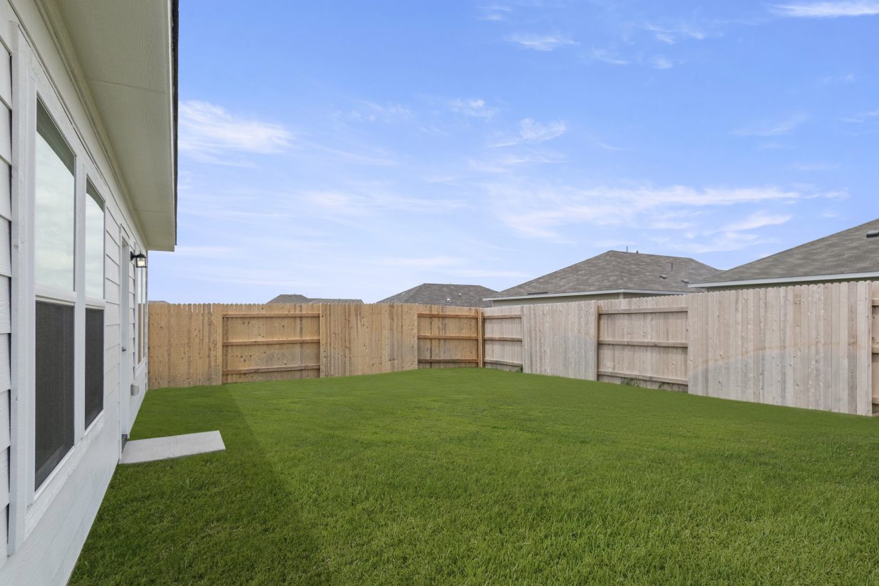 An image of a backyard with green grass, a light brown fence, and a blue sky background.