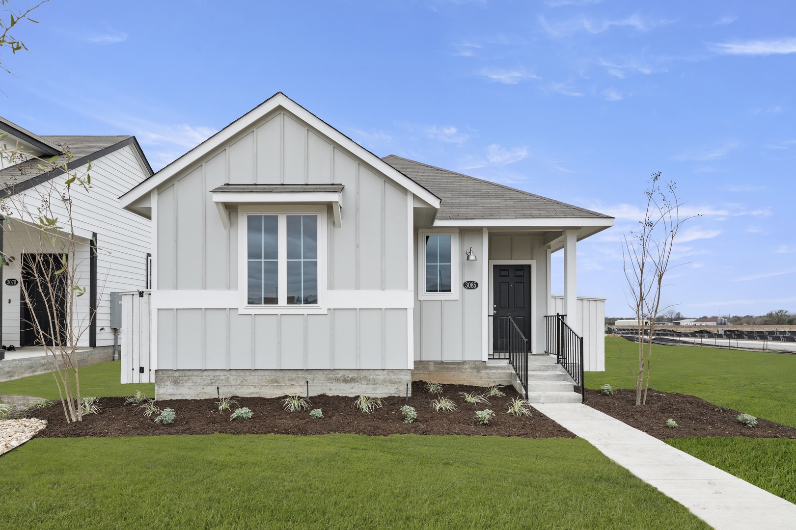 Image of a light grey one story house with white trim, windows, a black front door, a green grass front yard and a blue sky in the background
