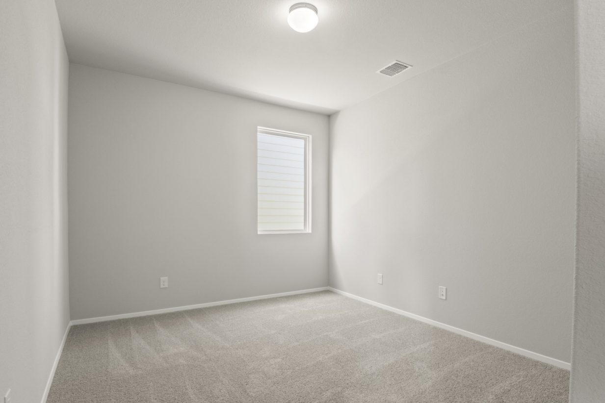 Image of a bedroom with tan carpeting and light grey painted walls with windows
