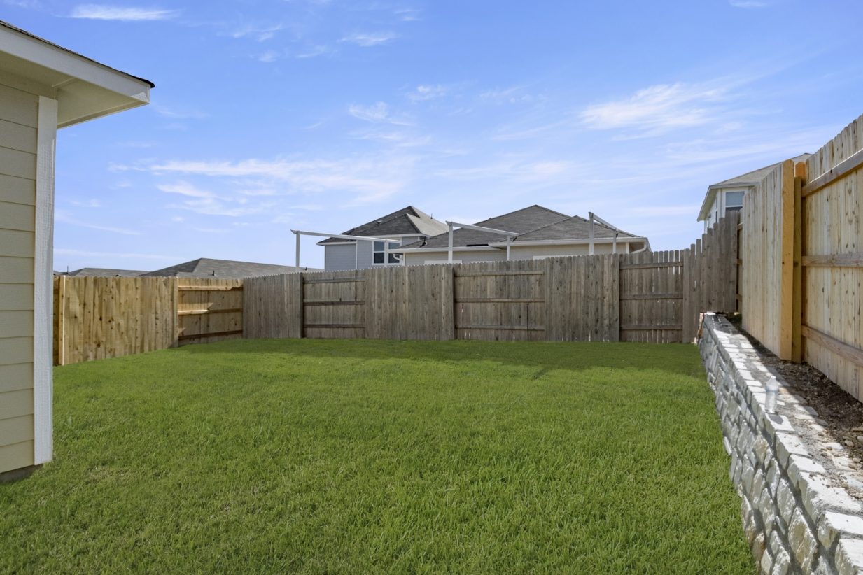 Image of a backyard with green grass and a wooden fence with a blue sky