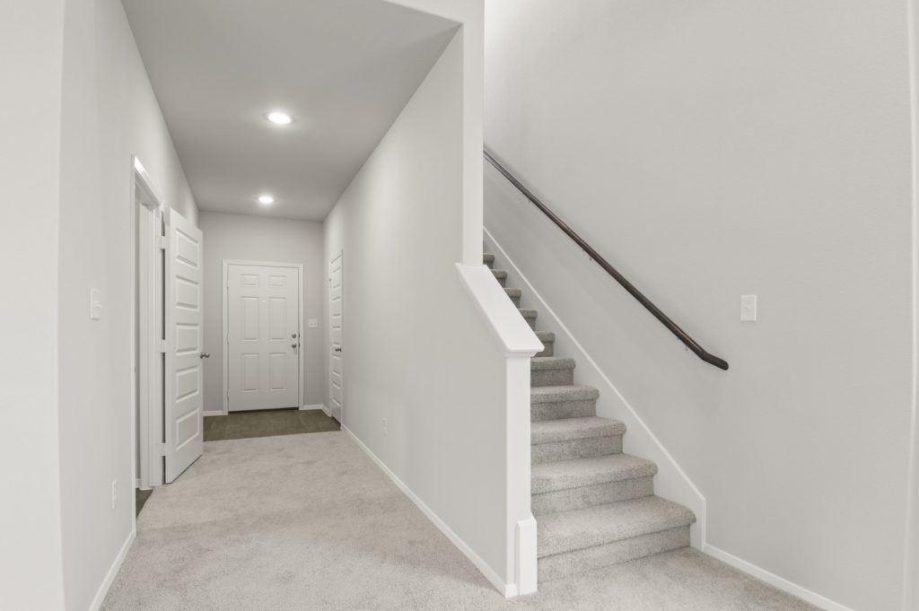 Image of a two story home with light grey carpeting and painted walls with a staircase that leads upstairs