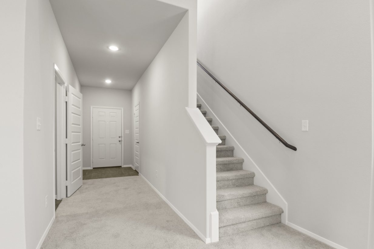 Image of a two story home with light grey carpeting and painted walls with a staircase that leads upstairs