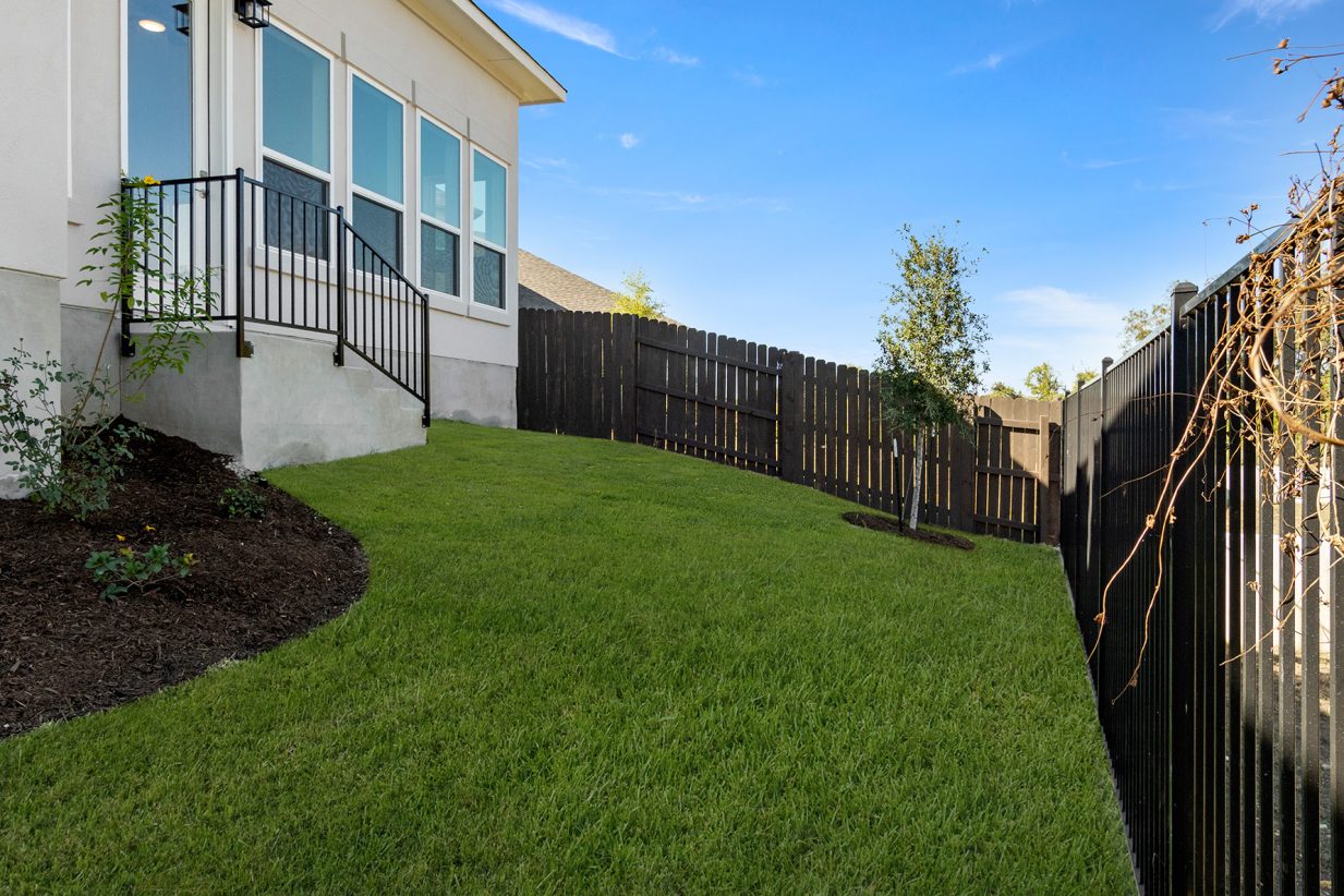 Image of back exterior two story home with a green grass backyard, black fence and a blue sky