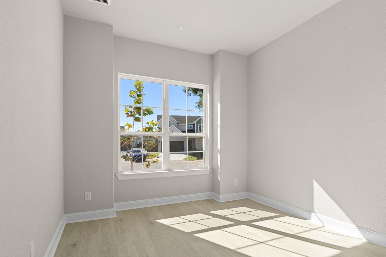 Image of a one story home bedroom with light brown wood-like floors and light grey painted walls with a large window