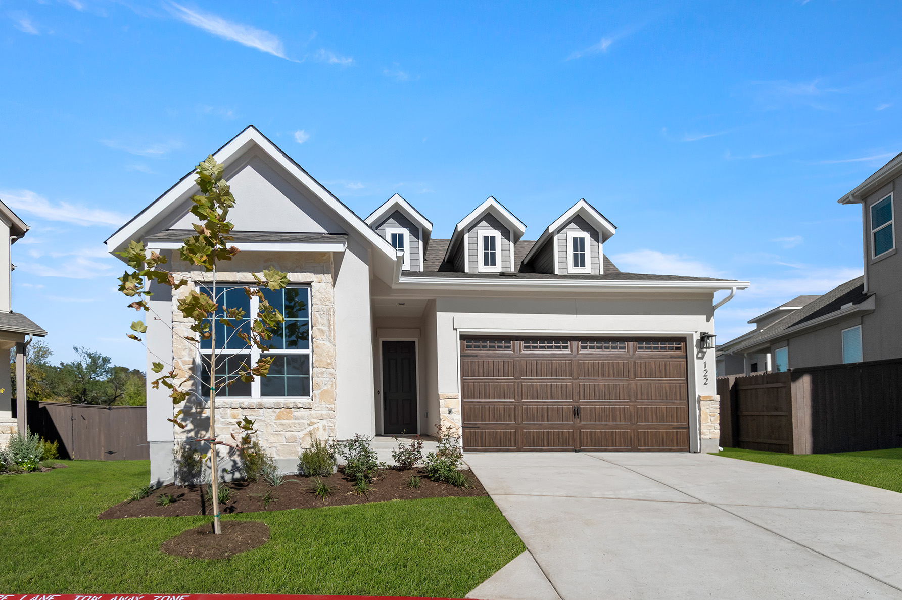 Front exterior of gray and brick accented single-story house with a brown two-car garage and grass landscape.