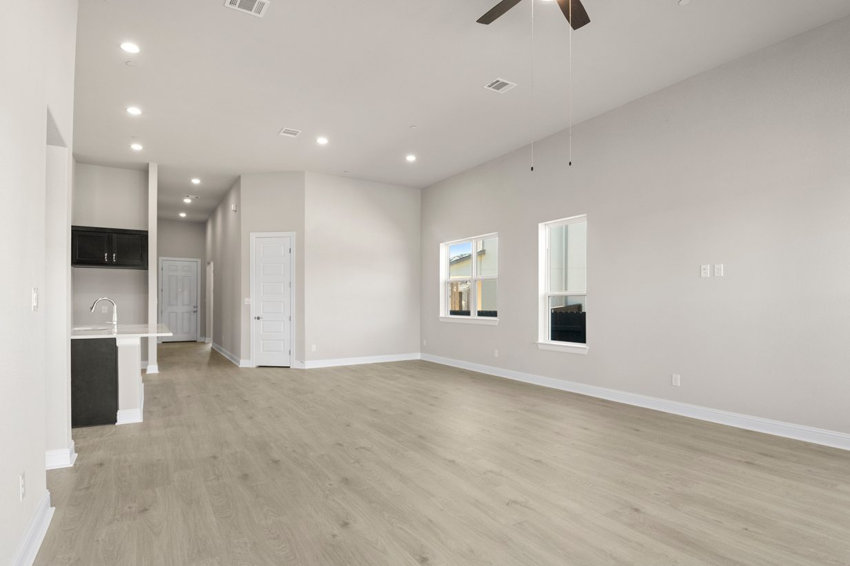 Image of a one story home living room with light brown flooring and light grey walls with a window and ceiling fans