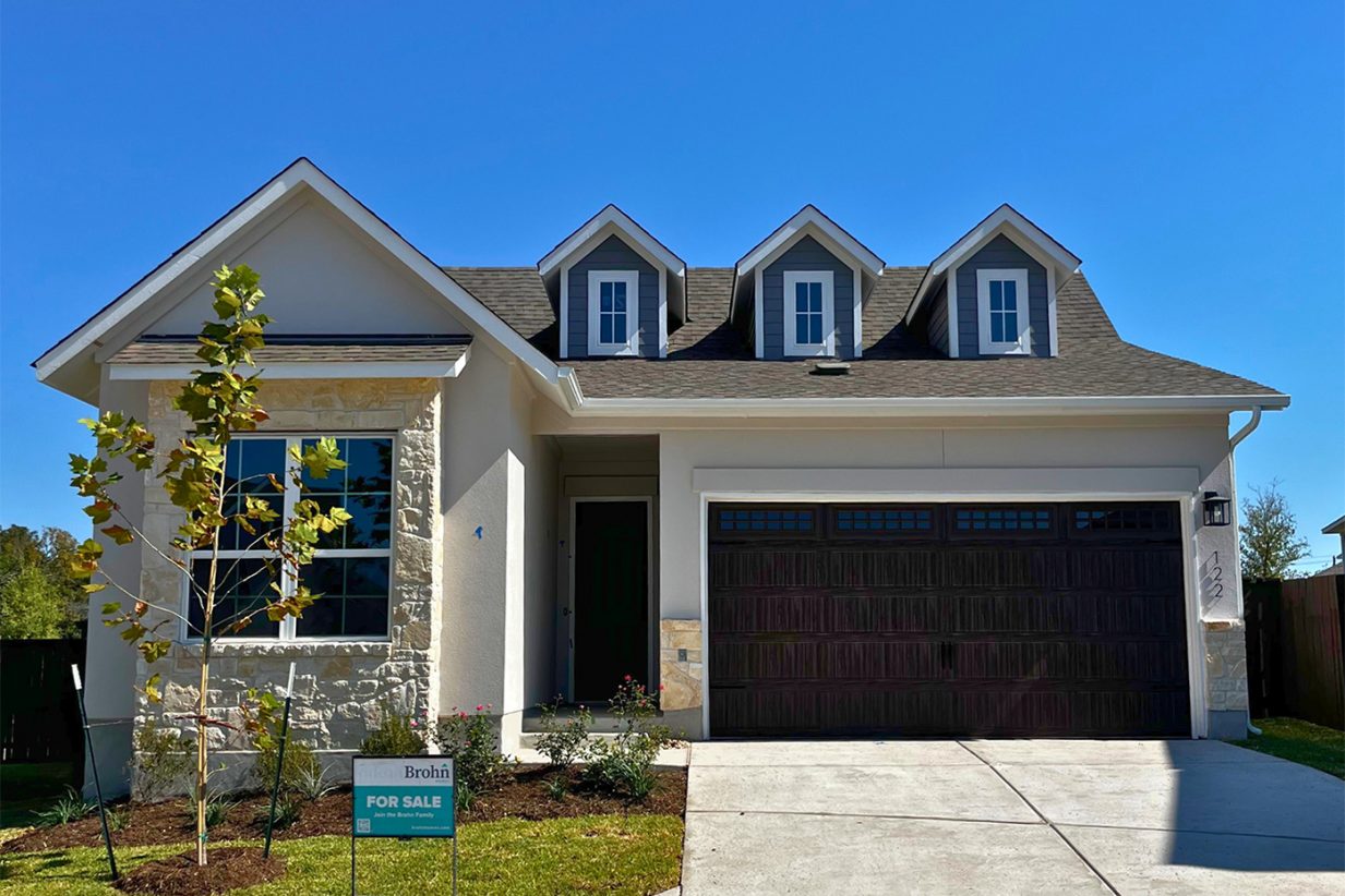 Front exterior of gray and brick accented single-story house with a brown two-car garage and grass landscape.