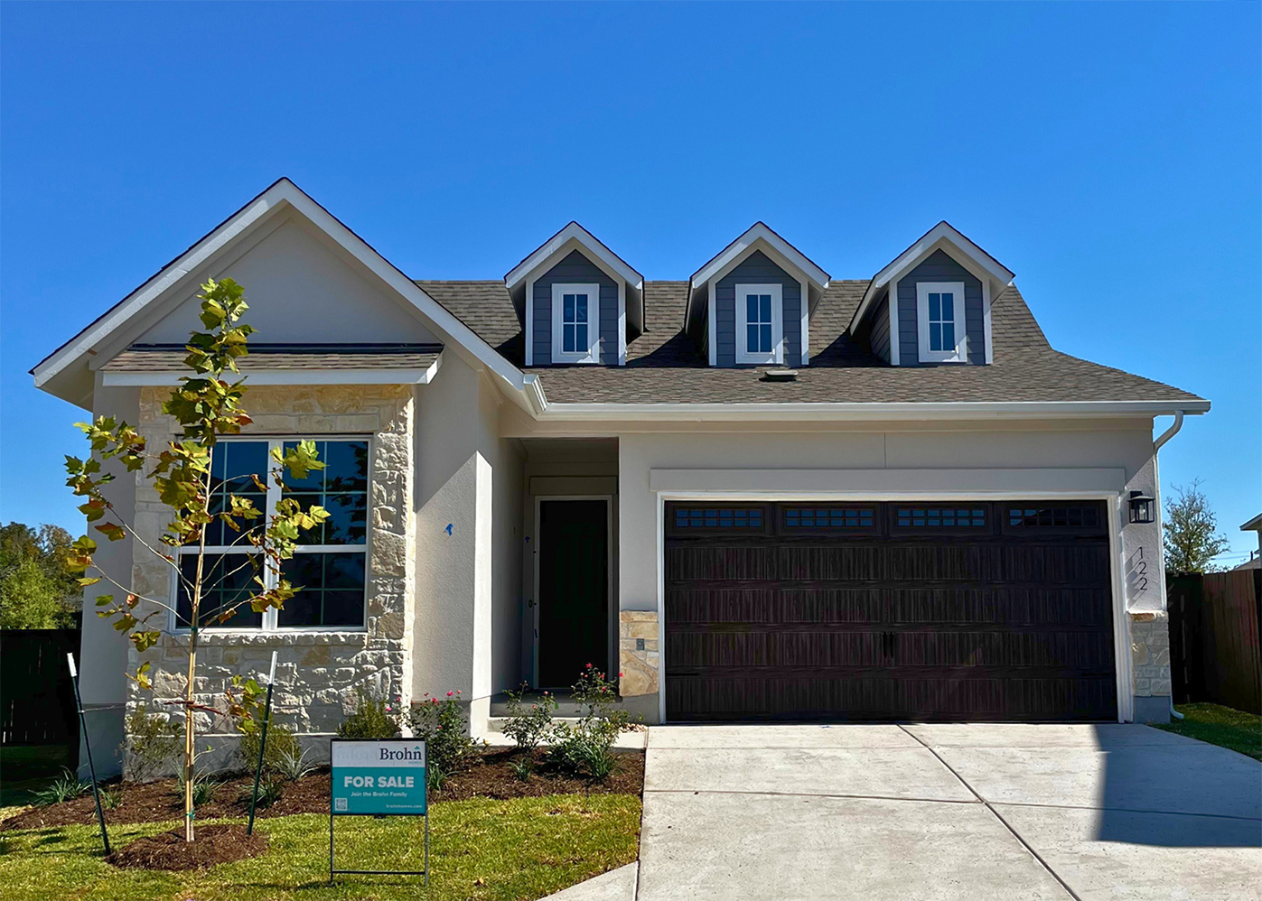 Front exterior of gray and brick accented single-story house with a brown two-car garage and grass landscape.