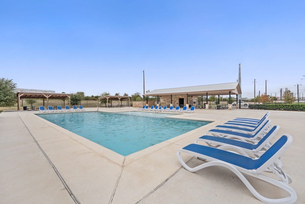 Image of a community swimming pool with blue lawn chairs along the pool