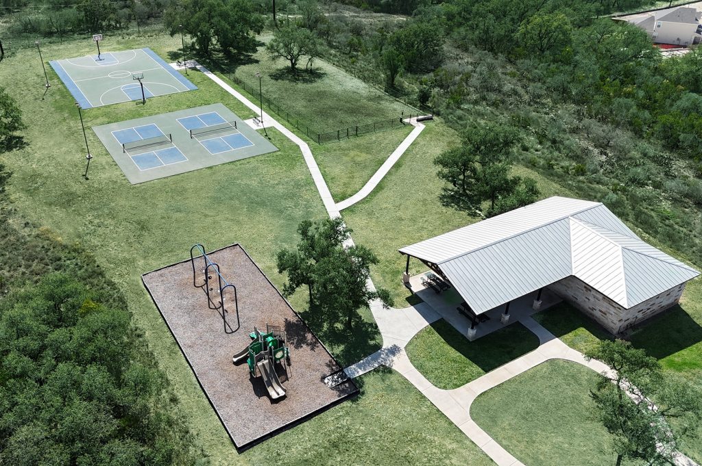Aerial photo of community amenity center including a pavilion, playground, and sports courts with trees and grass