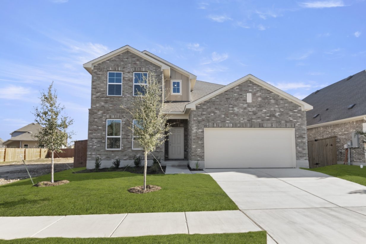 Image of a two story brick home with a two car garage and a cement driveway with green grass and a blue sky