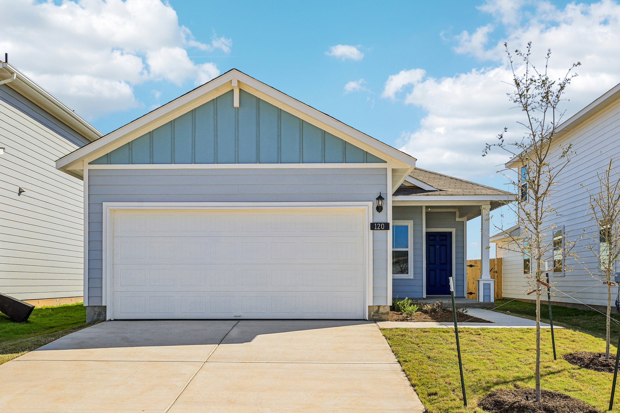 Image of a blue one story house with a white garage and cement driveway