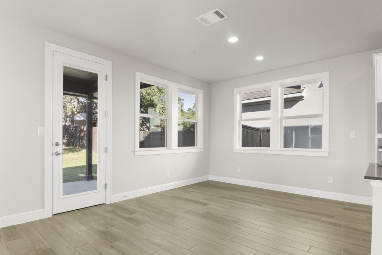Image of a dining room with wood-like flooring and light grey painted walls with a glass door leading to the backyard