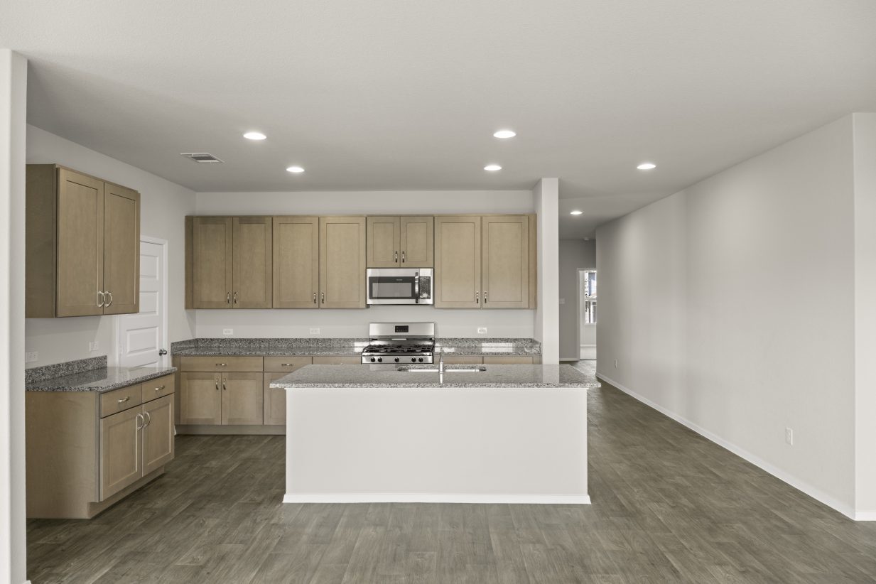 Image of home kitchen with light brown cabinets, center island, wood-look floors and white walls with entry way to the right