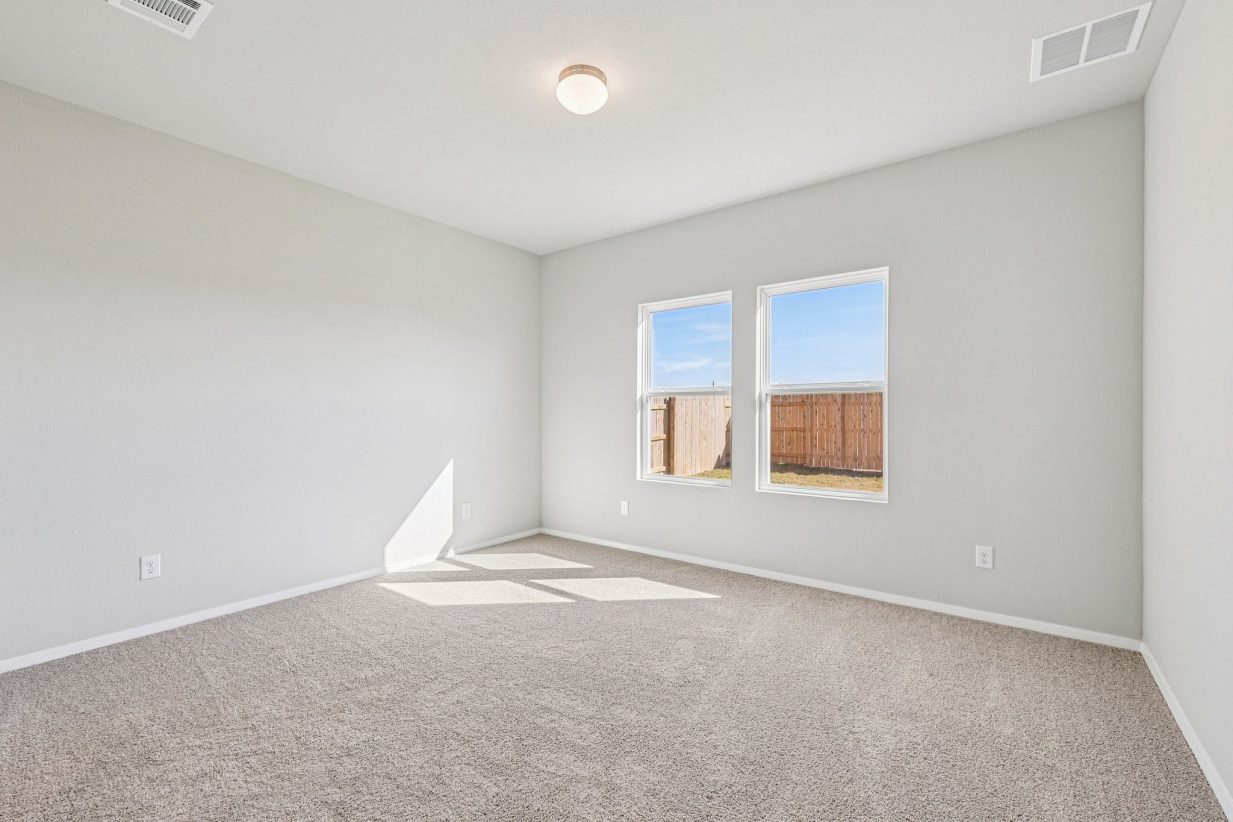 Image of a primary bedroom with beige walls, tan carpeting and windows