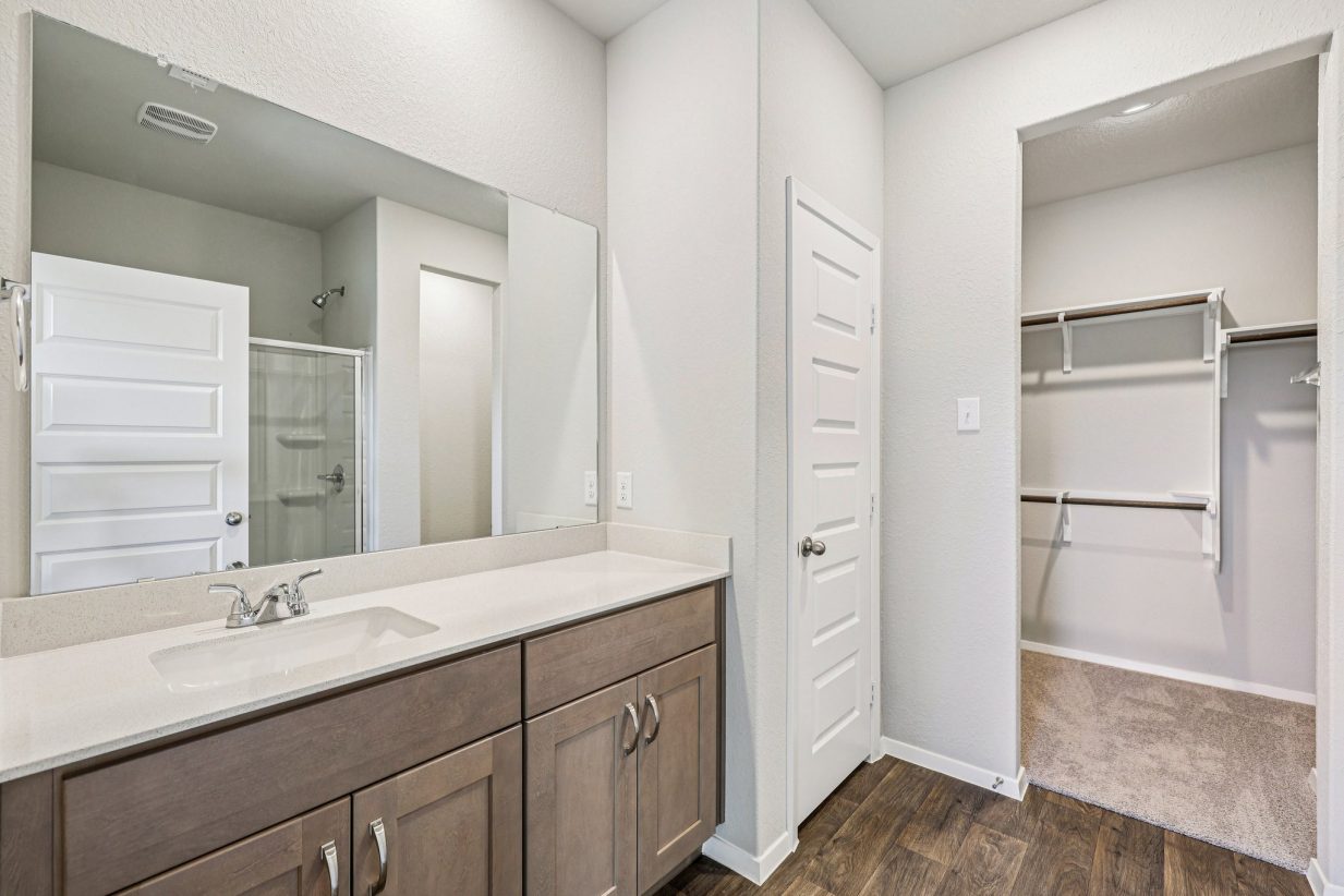 Image of a primary bedroom with a double vanity, brown cabinets, and a large mirror