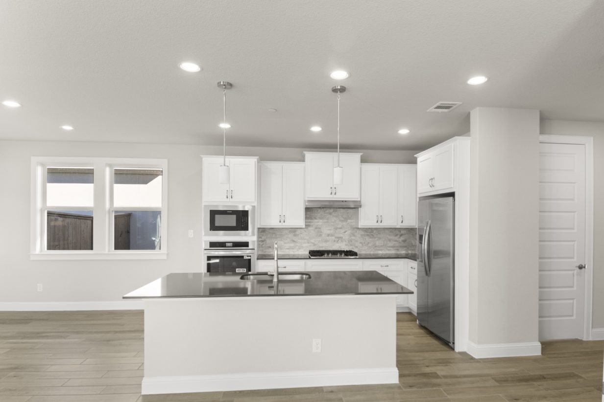 Image of a kitchen with white cabinets and a center island with stainless steel appliances and marble-like backsplash