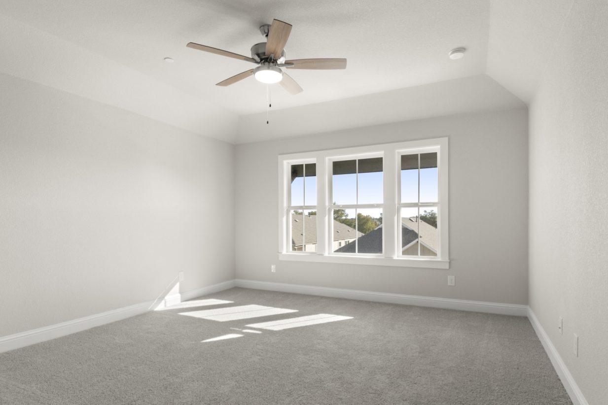 Image of a primary bedroom with light grey carpeted floors and painted walls with a ceiling fan and three windows with white trim