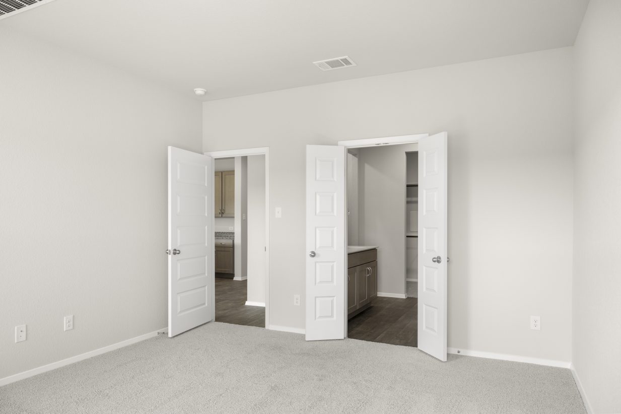 Image of home primary suite with door to main areas and one door to bathroom. Light carpet and white walls and doors