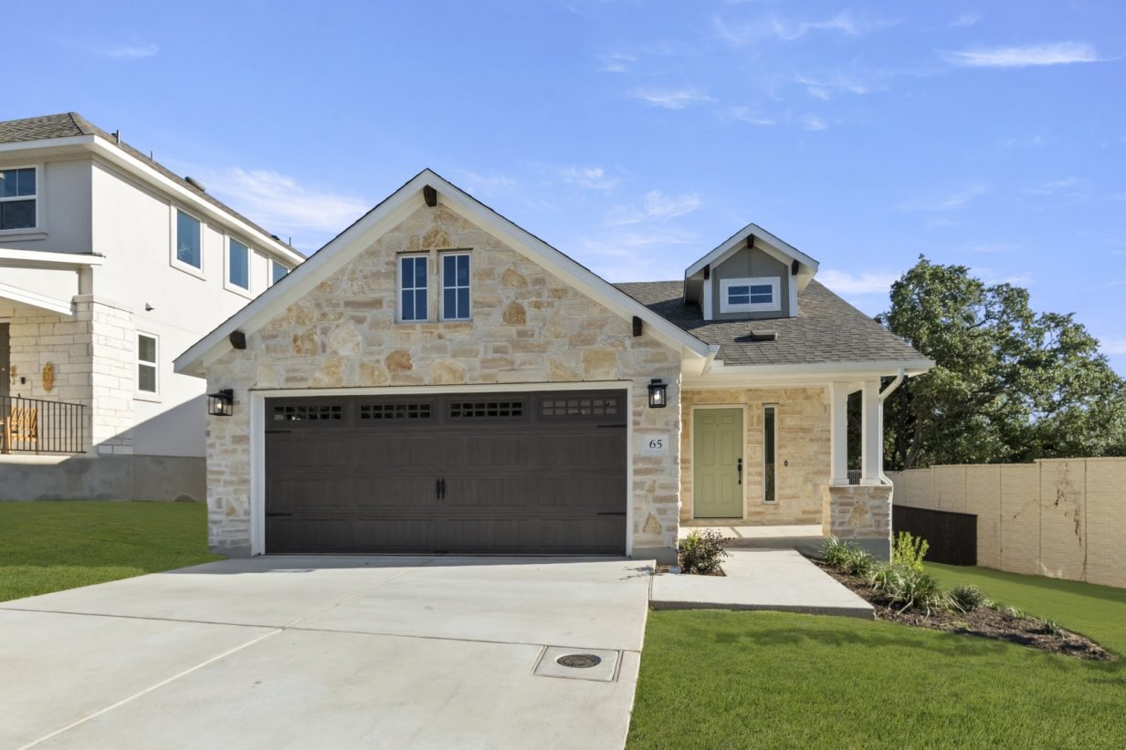 Front exterior image of brick house with brown garage door, driveway, and green landscape.