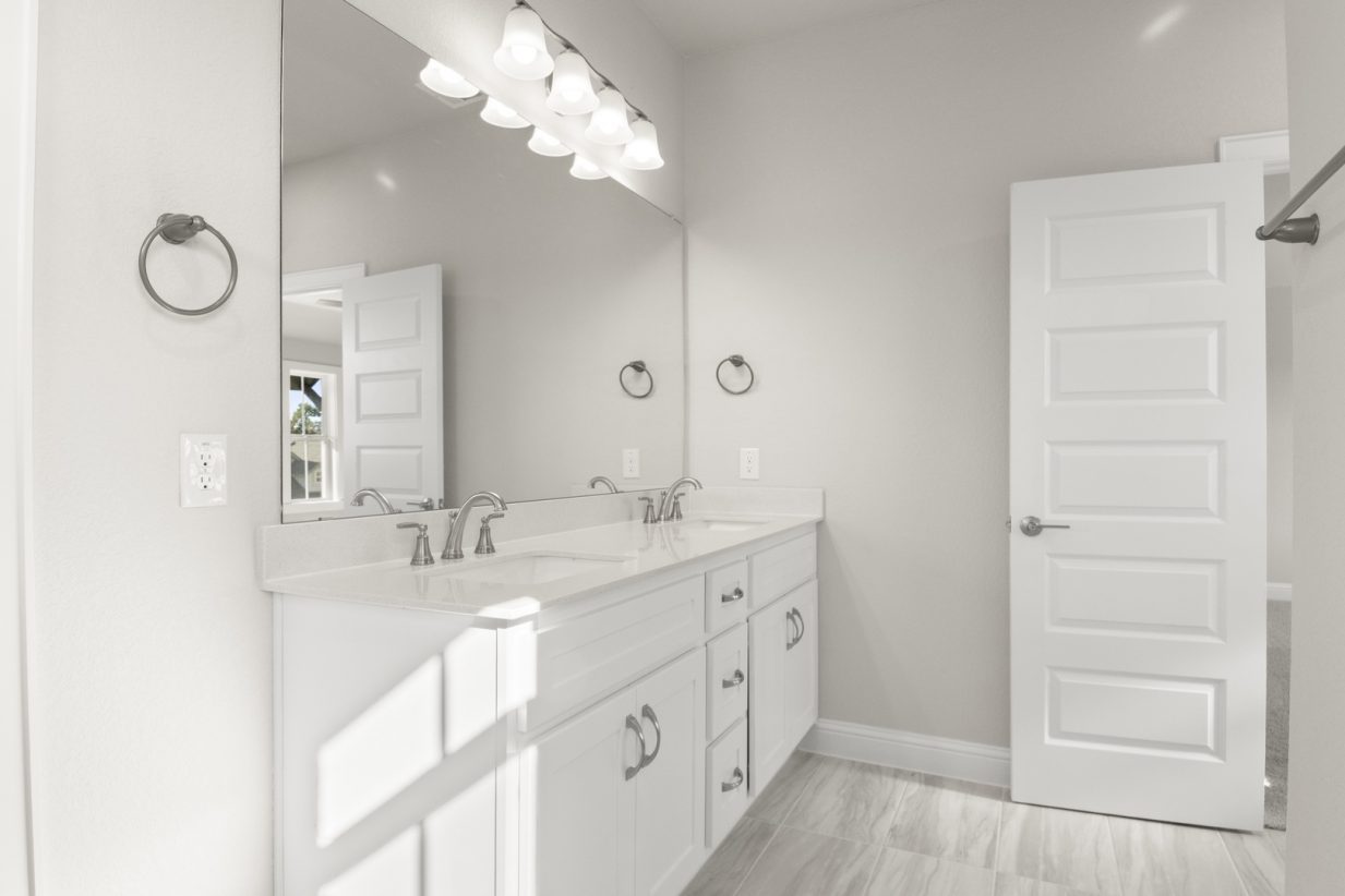 Image of a primary bathroom with white cabinets and a jack and jill vanity with a large mirror