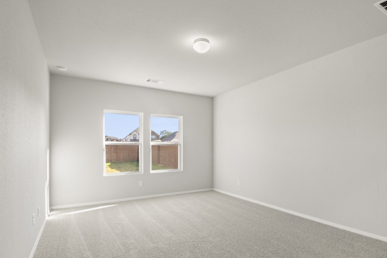 Image of a primary bedroom with tan carpeting and light grey painted walls with two windows