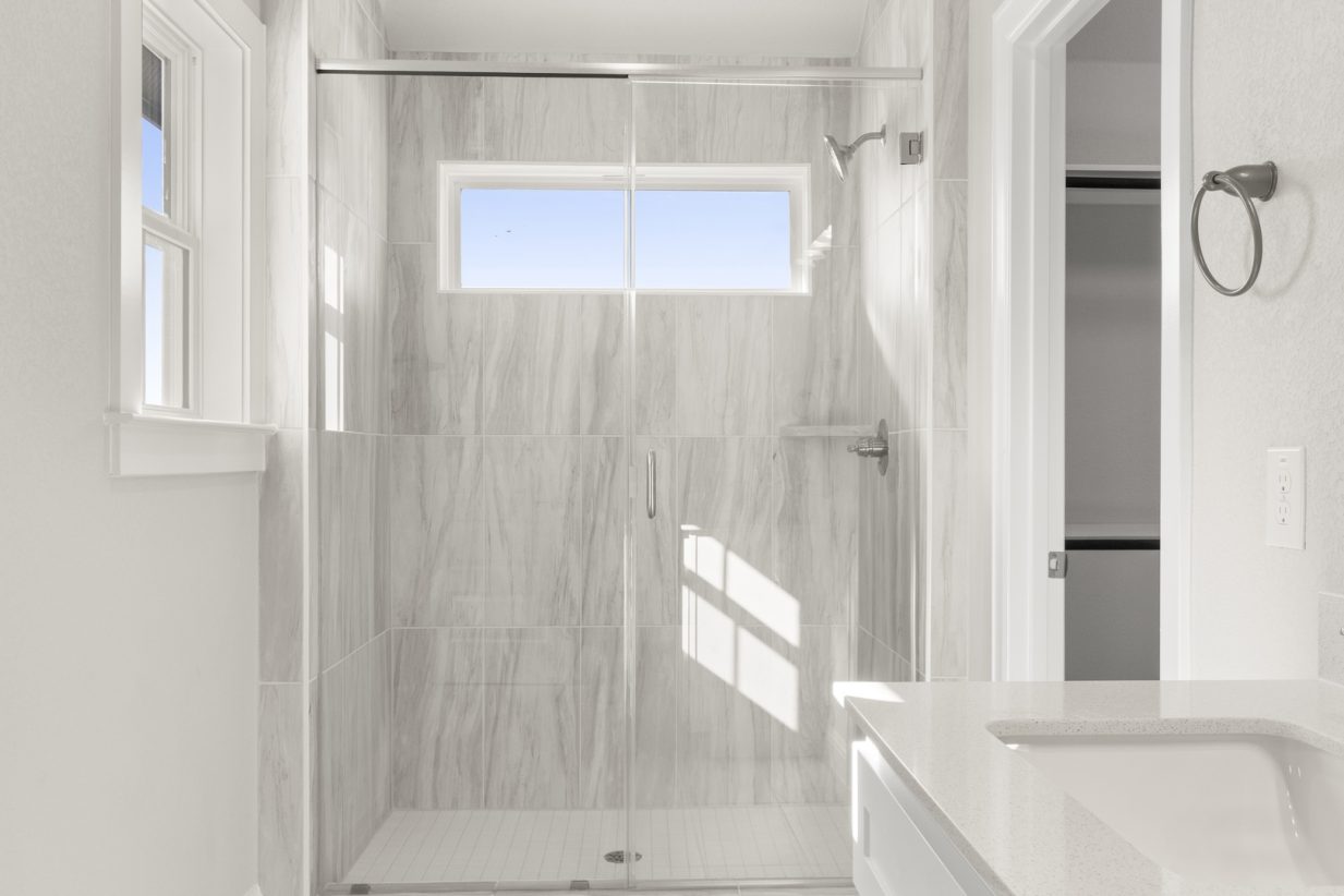 Image of a primary bathroom with a walk-in shower with a glass door and grey marble-like tile