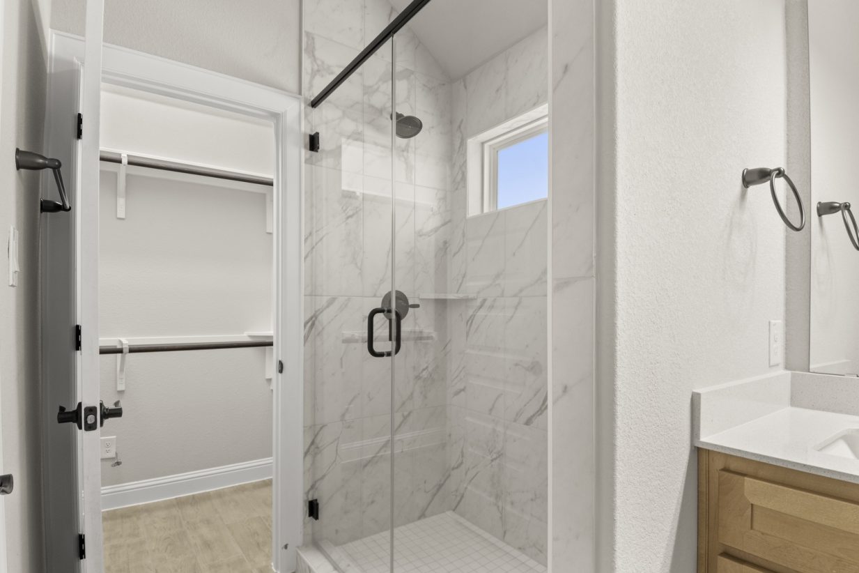 Image of primary bathroom with a marble tiled walk-in shower with a window and a connecting walk-in closet