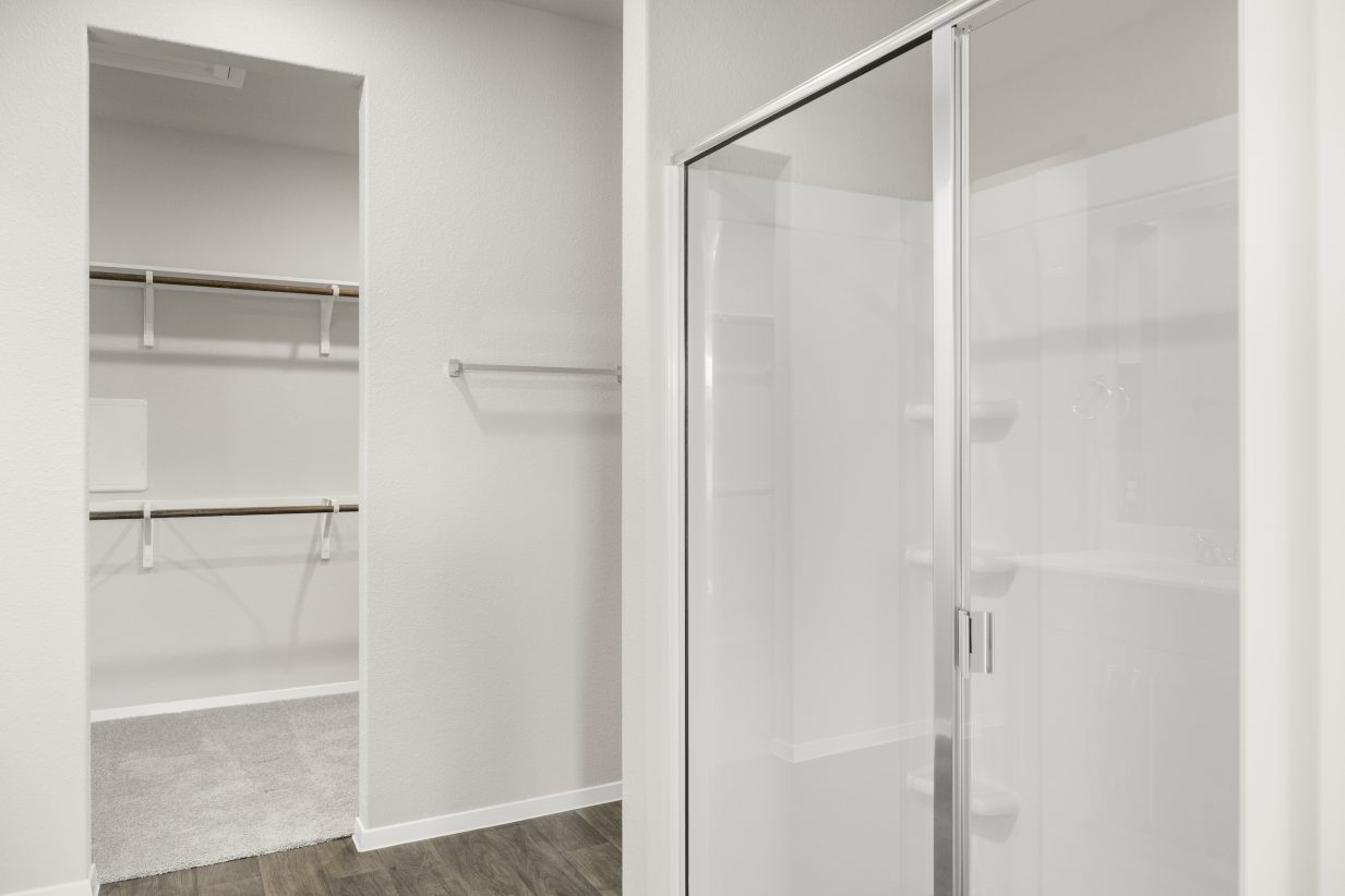 Image of home primary bathroom with walk-in shower with glass enclosure, towel bar, and doorway to walk-in closet