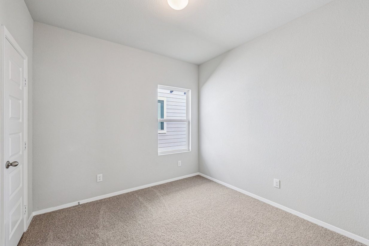 Image of a secondary bedroom with beige walls, tan carpeting and a window