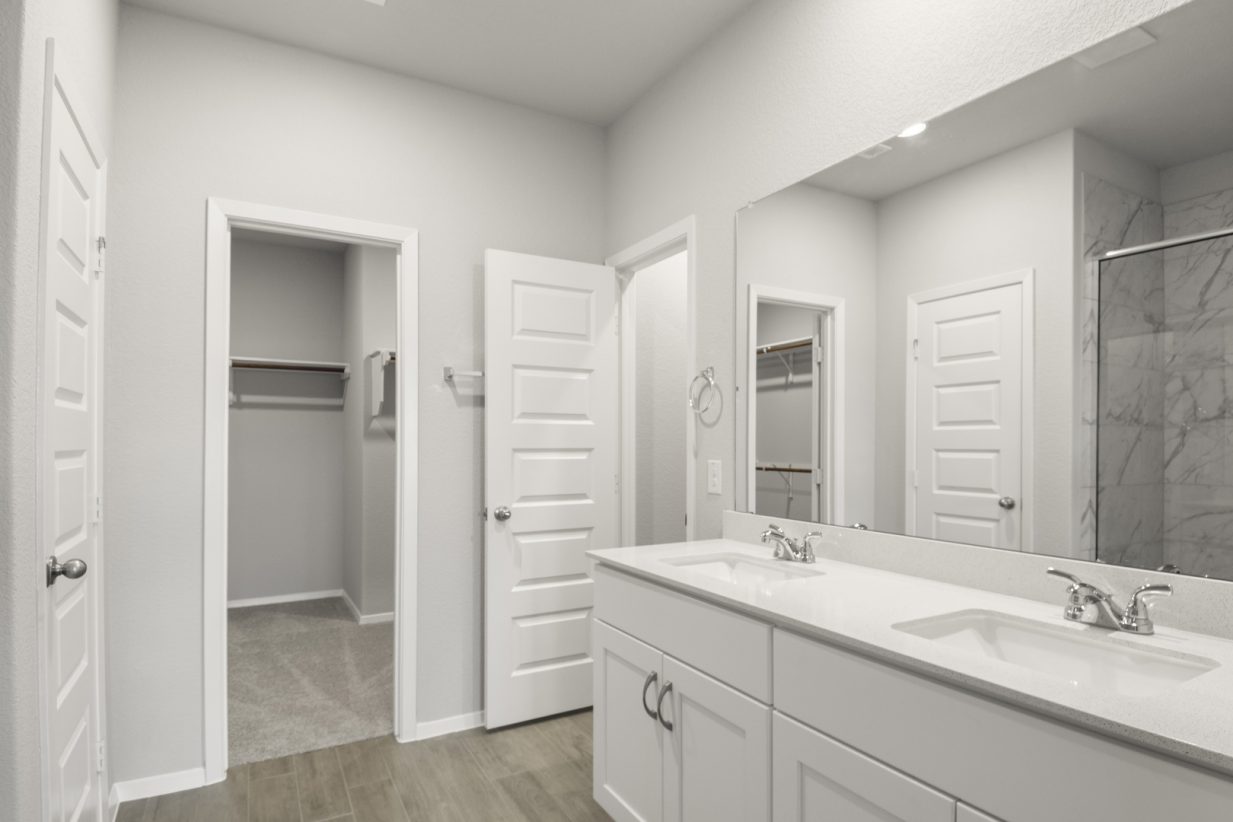 Image of a primary bathroom with white cabinets and a jack and jill vanity with a connecting walk-in closet
