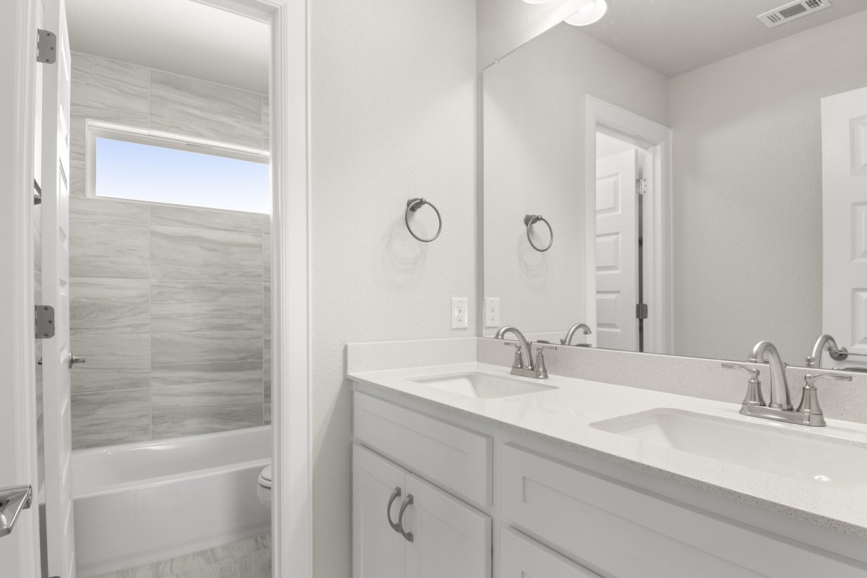 Image of a bathroom with white cabinets and jack and jill vanity with a large mirror and a private water closet with a shower and window