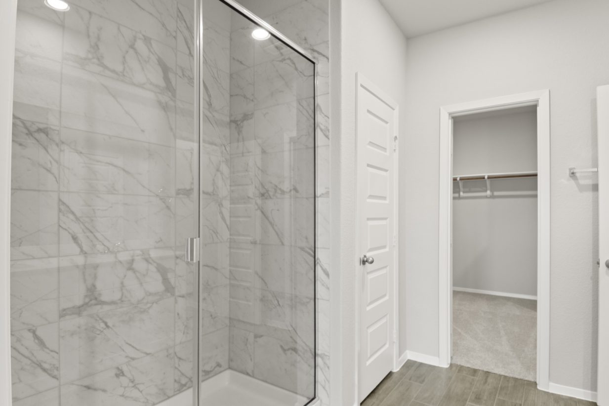 Image of a primary bathroom with a standing walk-in shower and marble-like tile with a connecting walk-in closet