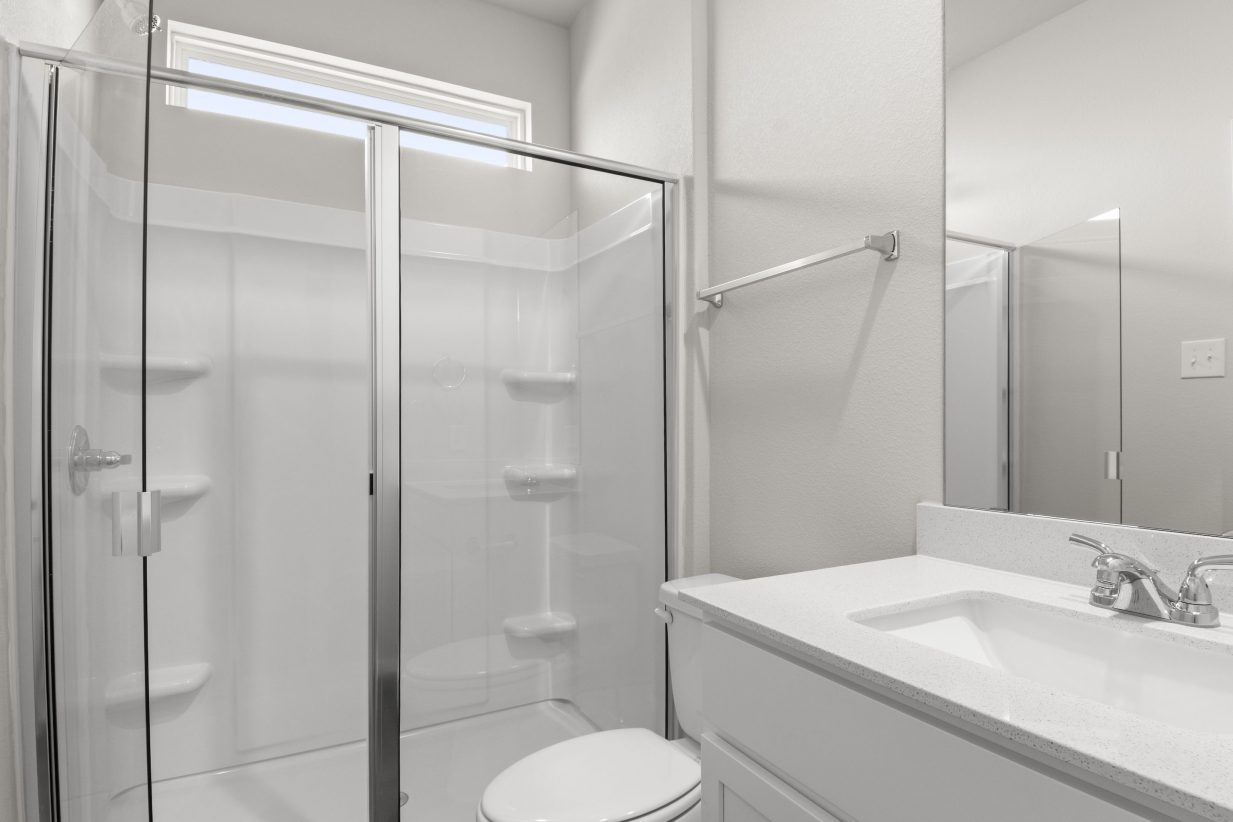 A bathroom with white vanity with white countertops, a mirror, and a walk-in glass shower, and white toilet.