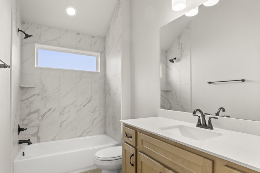 Image of a bathroom with a large white vanity and mirror, a marble tiled shower with tub, and light brown cabinets