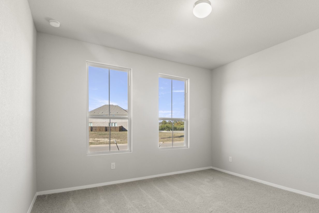 Image of a bedroom with tan carpeting and light grey painted walls with two windows
