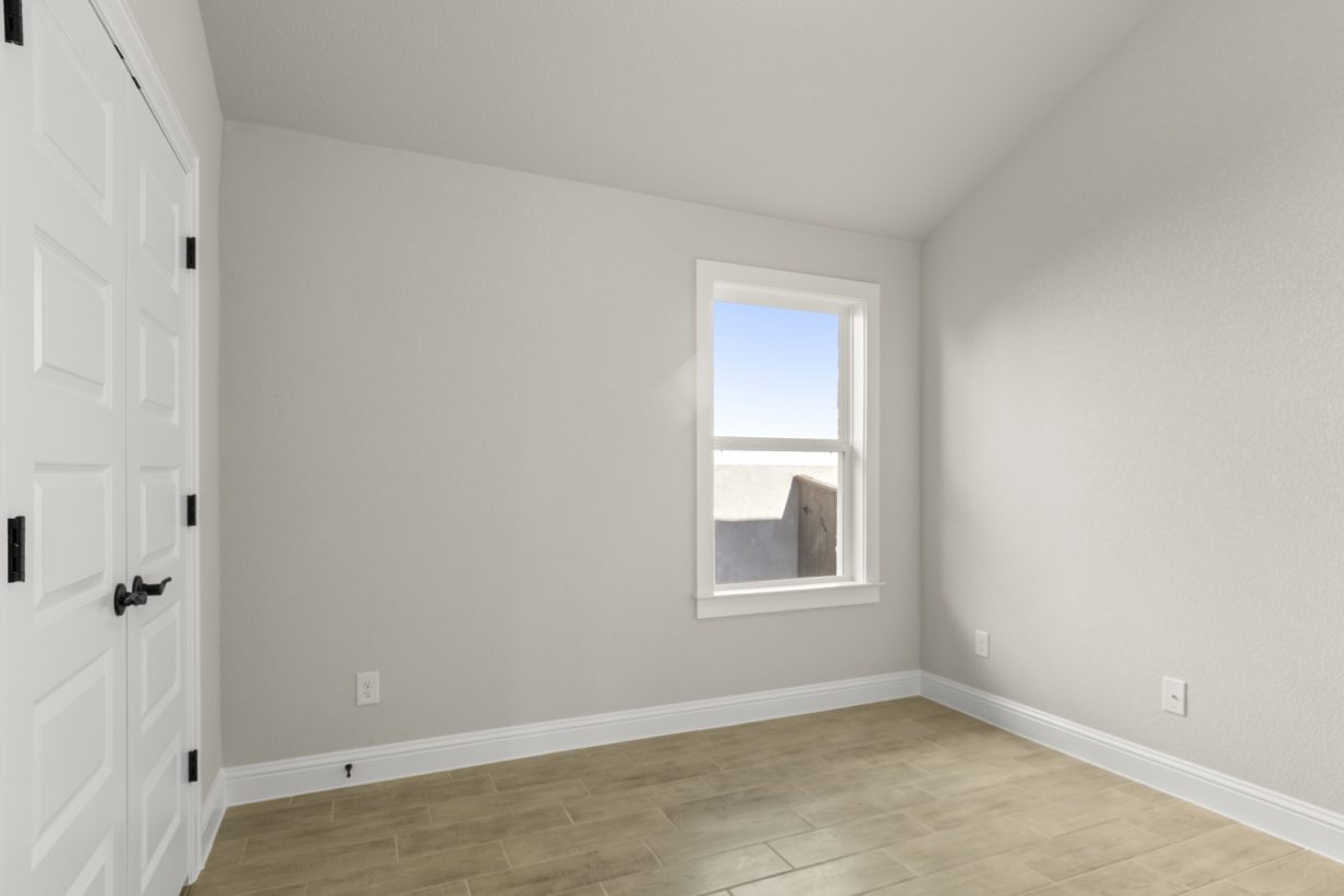 Image of a one story home bedroom with light wood-like flooring and light grey painted walls with a window in the corner