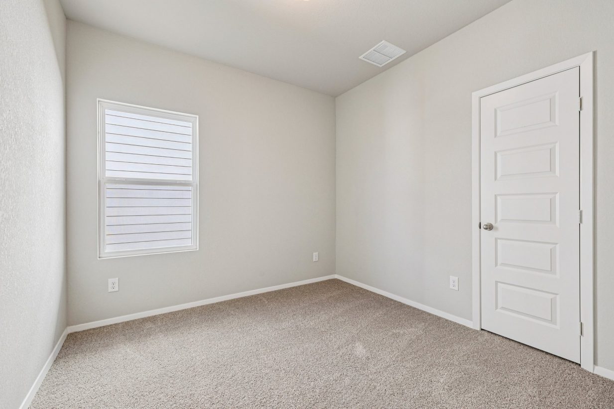 Image of a secondary bedroom with beige walls, tan carpeting and a window