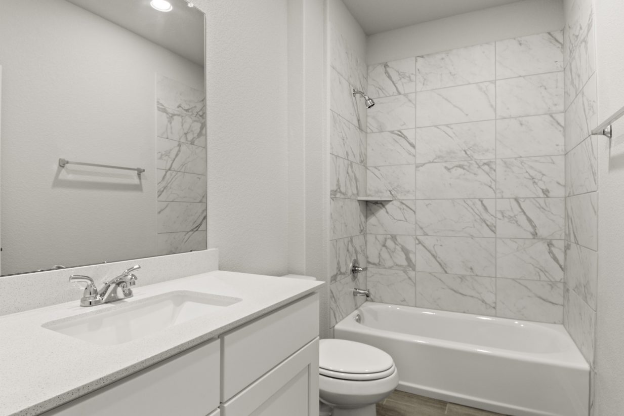 Image of a bathroom with white cabinets and a white vanity with a large mirror, a shower with a white vinyl tub and marble-like tile